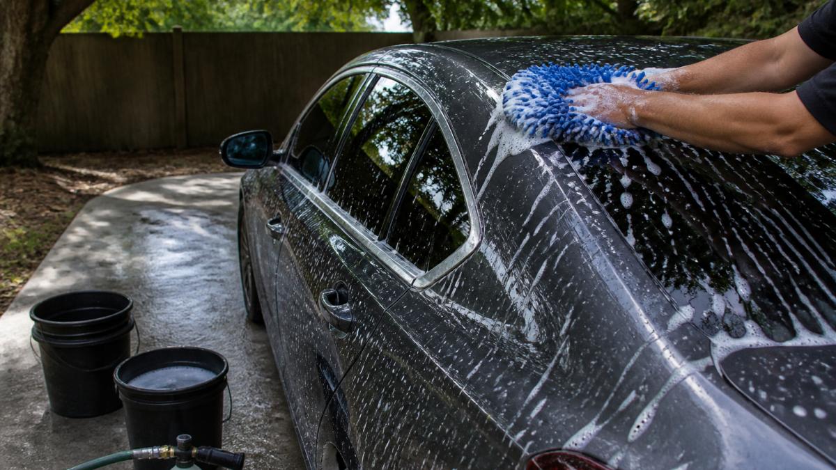 Hands using a microfiber mitt to wash a car exterior in the shade